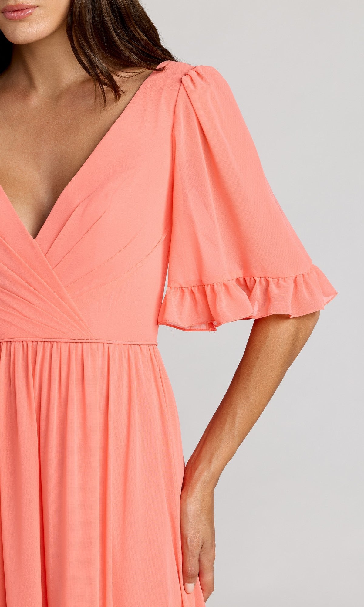 A woman wearing Mac Duggal’s Long Formal Dress 55867: coral pink, a-line with deep V-neckline, puffed short ruffled sleeves, and a gathered waist.